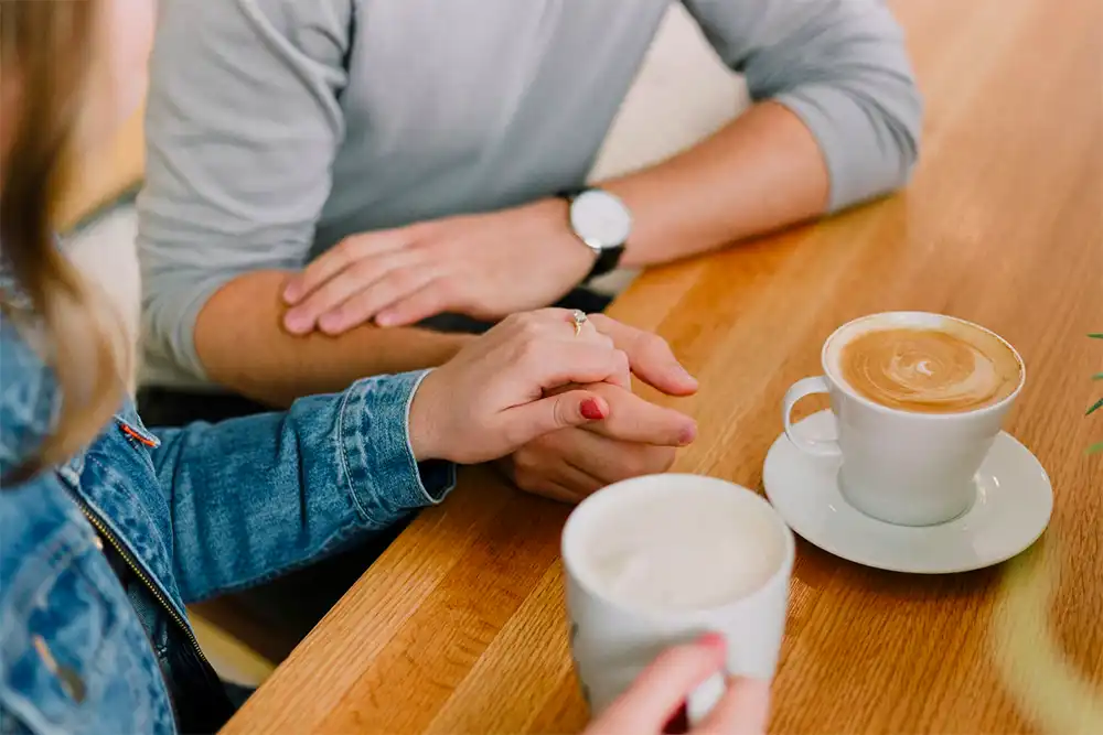 Man and woman holding hands of each other while drinking coffee